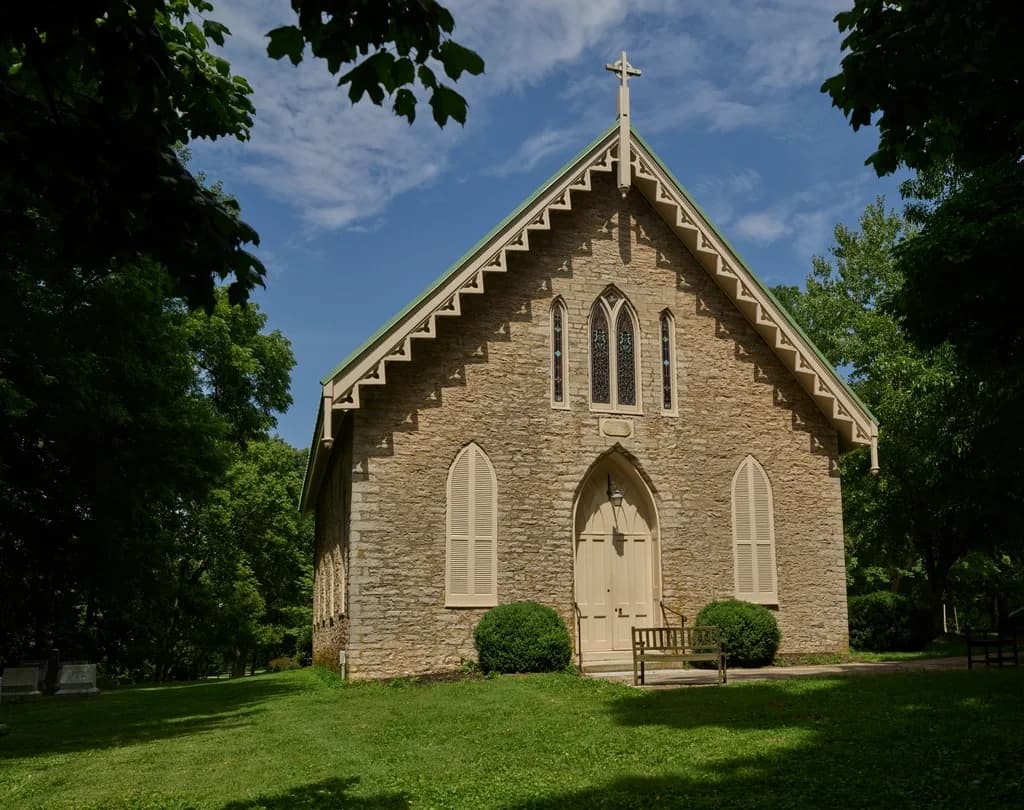 Stone country church with white trim and a bench by the front door on a sunny morning