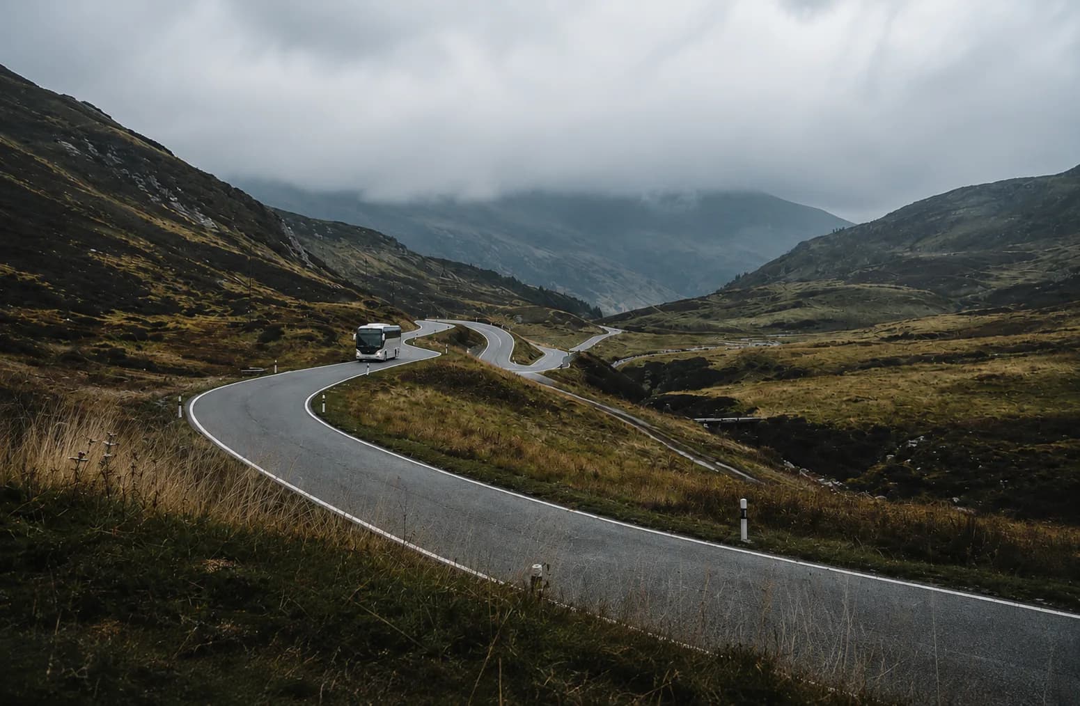 A charter bus descending a misty mountain pass road through switchback turns