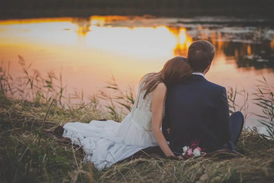Bride and groom sitting together at the water's edge as the sun sets after the ceremony