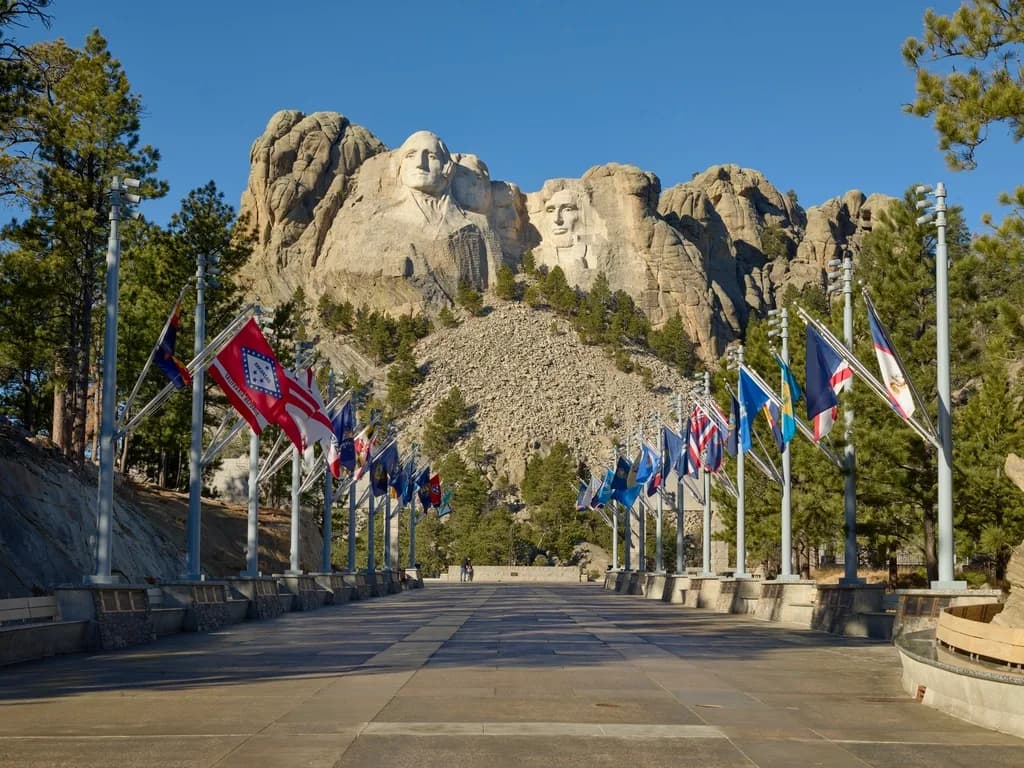 The Avenue of Flags leading toward the carved presidential faces of Mount Rushmore on a clear morning