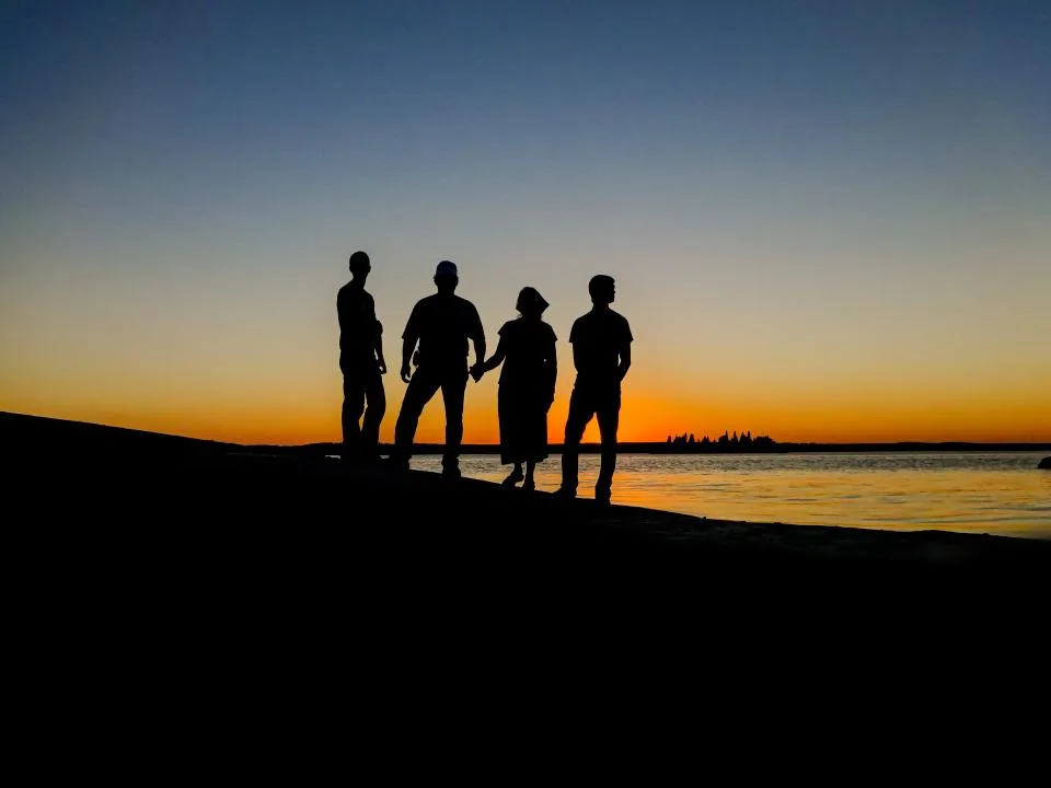 Family of four silhouetted against an orange sunset at the waterfront on a group outing