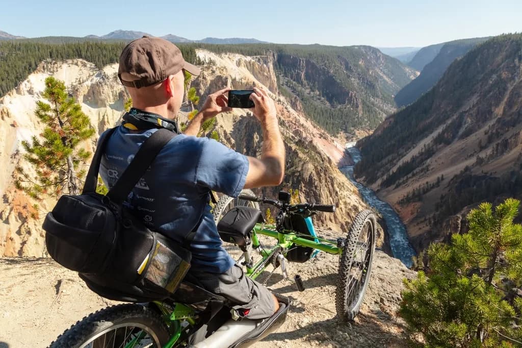 Rider on an adaptive handcycle pausing at a canyon overlook to photograph the river below